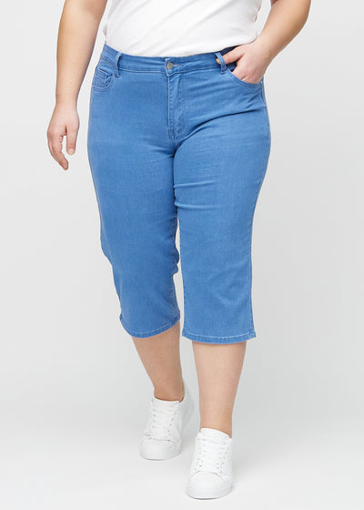 Blå regular capris, modelnavn Geraniums, som sidder lige til benet og slutter lige under knæet på en plus-size model, set forfra.