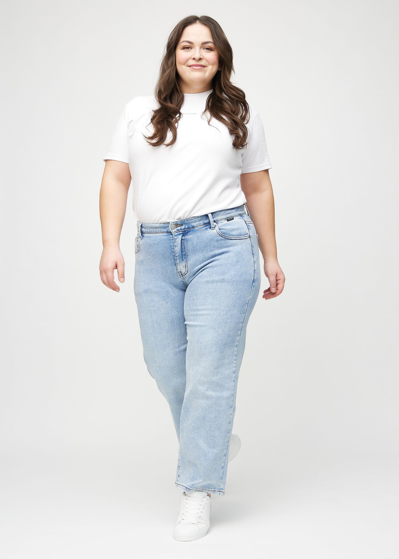 Plus-size model går ind i billedet, strækker i jeansene, viser dem frem ved at dreje rundt, og forlader derefter billedet.